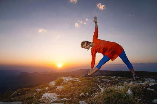 woman in warrior pose in mountains, yoga practice outdoors at sunset.