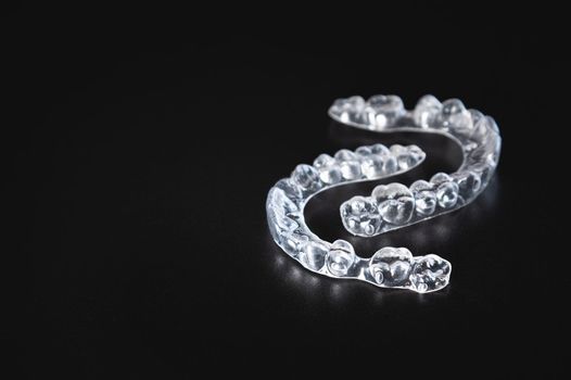 a pair of transparent braces lies on a black background. orthodontics, bite correction and cometic dental care.