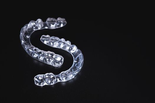 a pair of transparent braces lies on a black background. orthodontics, bite correction and cometic dental care.