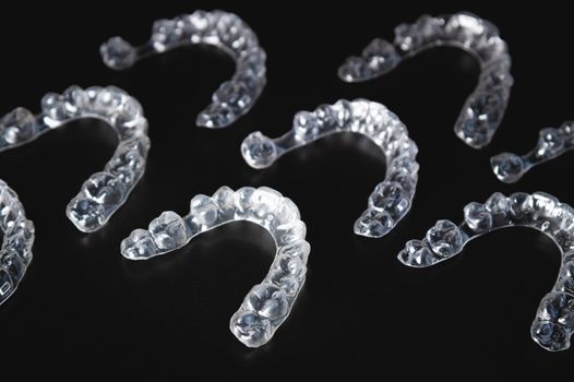a pattern of invisible plastic aligners lie on a black background.
