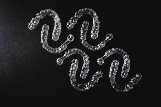 a pattern of invisible plastic aligners lie on a black background.