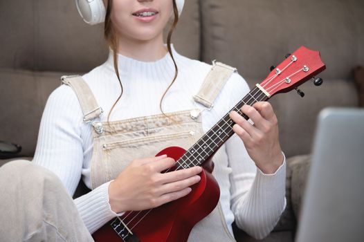 close-up, a woman or girl plays the ukulele while sitting at home, on the floor. distance learning.