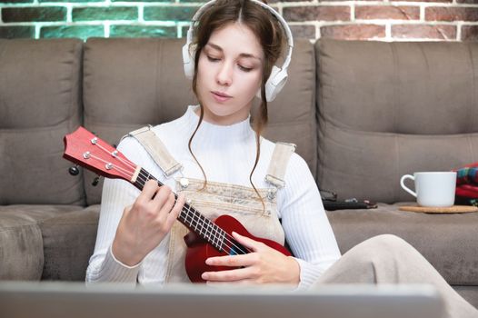 young female student learning to play the ukulele at home, distance learning vocal and musical instrument.