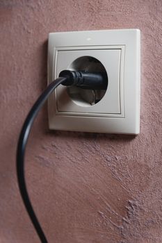 White electrical outlet on the wall with a black wire inserted. close-up, home decor.