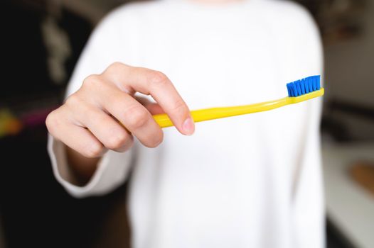 a bright toothbrush in female hands in the foreground, the background of the room is blurred.