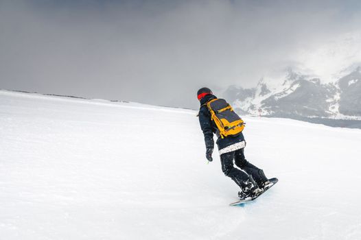 Freeride snowboarder rolls down a snowy slope, leaving behind a trail on the background of mountains, downhill, winter sport.