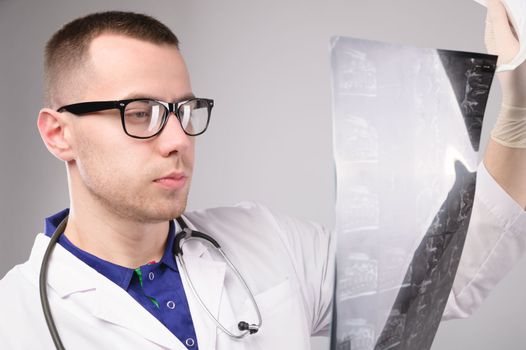 Young male doctor looking at an x-ray in a hospital on a white background, portrait of a specialist in uniform.