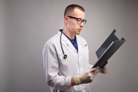 Portrait of a confident doctor in uniform and glasses holding a folder and looking into it with a serious face.