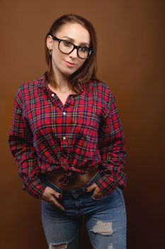 Smiling brunette in glasses posing with her hands in her jeans pockets and looking at the camera, studio.