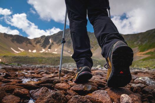 Hiking boots close-up on mountain rocks by the lake with trekking poles, view from below.