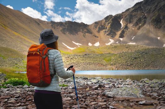 A woman with a backpack walks near the mountains and a blue lake. Travel and hobby concept. Back view