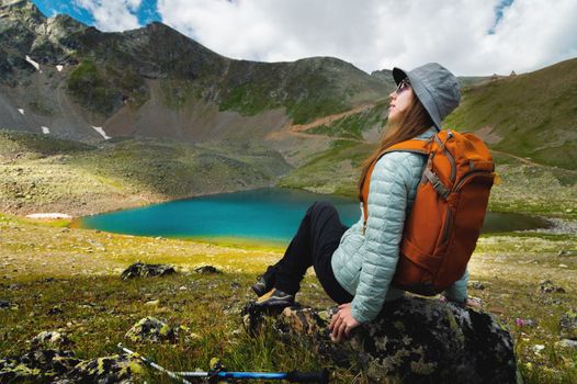 a woman tourist sits with a backpack with her back to the camera near a mountain lake. hiking vacation.