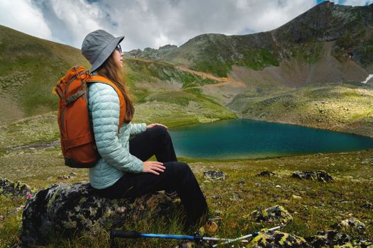 a woman tourist sits with a backpack with her back to the camera near a mountain lake. hiking vacation.