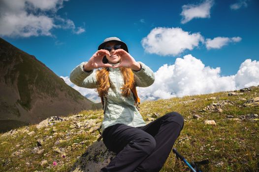 smiling young woman showing fingers gesture sign of heart, love in mountains, happy tourist.