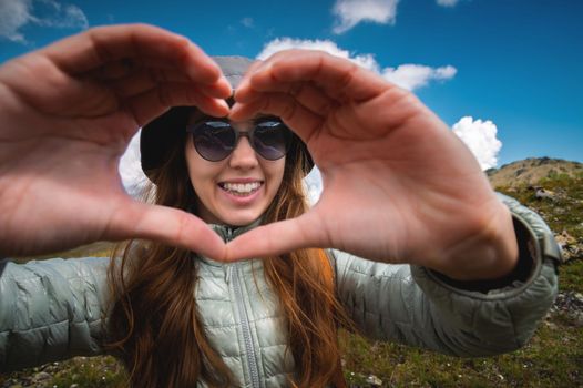 smiling young woman showing fingers gesture sign of heart, love in mountains, happy tourist.