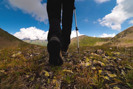 legs of a tourist in boots with trekking poles close-up, hiking in the mountains over stones.