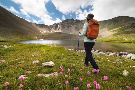 A woman with a backpack walks near the mountains and a blue lake. Travel and hobby concept.