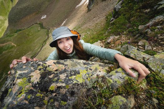 happy woman climbs a rock while trekking outdoors. carefree backpacker smiling at camera.