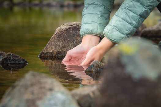 Close-up of water drops falling from female hands into a stream. The hand touches fresh water. A tourist drinks water from a reservoir in the mountains in summer on a sunny day.