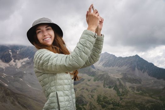 a woman takes pictures on a mobile phone of the mountains surrounding her, smiles and enjoys the hike. happy tourist.