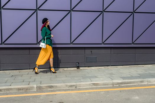 woman in bright clothes, yellow skirt and green jacket. Yellow socks in sandals, beret on the head, hair with the color of magenta.