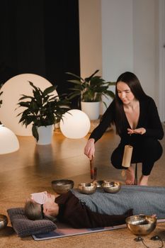 A young beautiful woman is doing a massage with singing bowls and a koshi bell to another girl. Sound therapy.