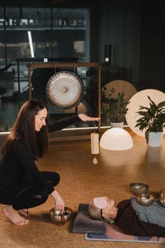 A young beautiful woman is doing a massage with singing bowls and a koshi bell to another girl. Sound therapy.