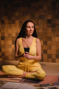 A girl in yellow clothes sitting on the floor holding pencils for drawing.