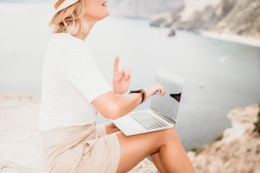 Digital nomad, Business woman working on laptop by the sea. Pretty lady typing on computer by the sea at sunset, makes a business transaction online from a distance. Freelance remote work on vacation