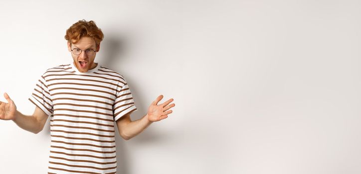 Impressed redhead man in glasses showing length of something big, demonstrate large size and looking amazed, standing over white background.