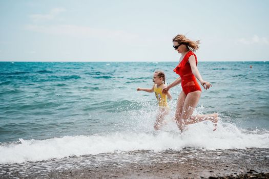 Happy loving family mother and daughter having fun together on the beach. Mum playing with her kid in holiday vacation next to the ocean - Family lifestyle and love concept.