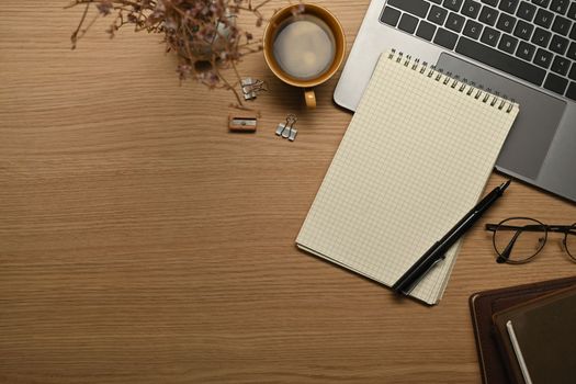 Empty notepad, eyeglasses, pen and laptop computer on wooden working desk. Top view with copy space.