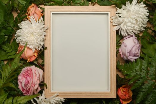 Blank picture frame surrounded by colorful spring flower and green leaves. Floral frame, spring or summer background.