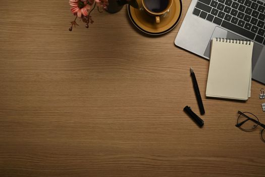 Top view of notepad, eyeglasses, laptop and cup of coffee on wooden working desk. Copy space for your text.