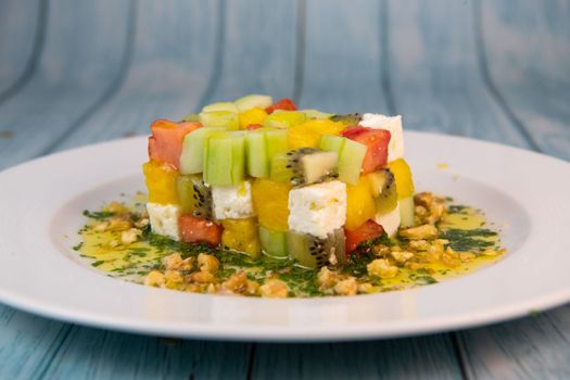 Recipe for sweet and sour salad, feta cheese, cucumber, tomato, kiwi, mango, oil and lemon sauce, parsley and nuts. High quality photo