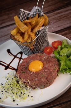 Steak Tartare with vegetables salad and french fries on dish. High quality photo