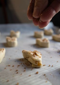 Woman hand sprinkling brown sugar on uncooked pastry palmeritas, also known as orejitas (little ears).