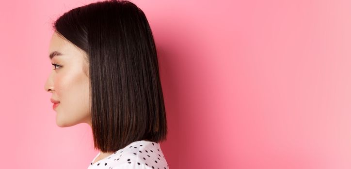 Beauty and skin care concept. Headshot profile of young beautiful asian woman with short dark hair, looking left at copy space, standing over pink background.