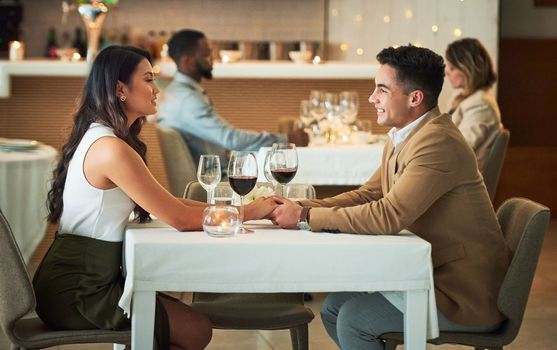 Couple in restaurant for dinner, holding hands and romantic date on Valentines day, love and celebrate holiday. Commitment, interracial relationship and man with woman, trust, support and celebration.