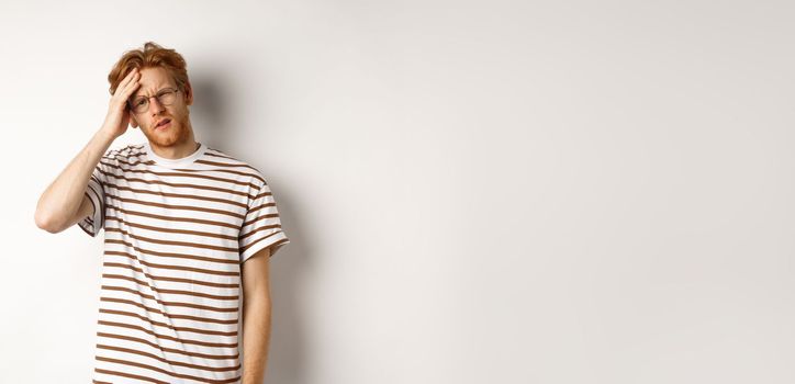 Tired young man student touching head, looking complex and tired, standing over white background.