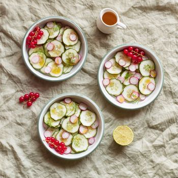 radish and cucumber salad served in three round bowls, decorated with red currants, top view