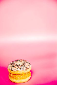 Sweet donuts stacked in a stack on a pink background. Copy space, various glaze and sprinkels chocolate chip, snack fast food sweets concept candy