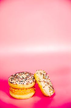 Sweet donuts stacked in a stack on a pink background. Copy space, various glaze and sprinkels chocolate chip, snack fast food sweets concept candy