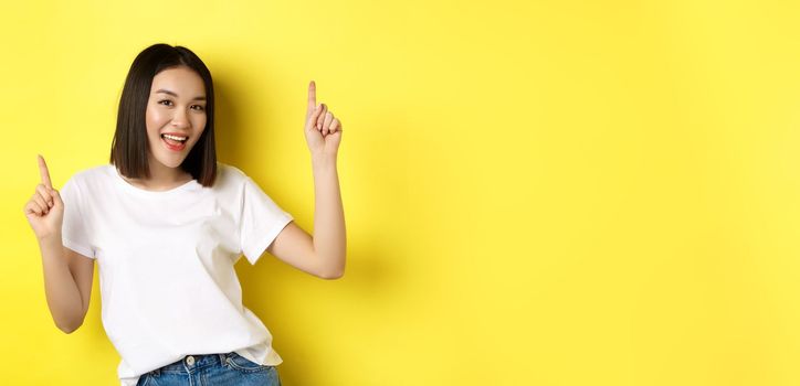 Happy asian woman dancing and having fun, posing in white t-shirt against yellow background.