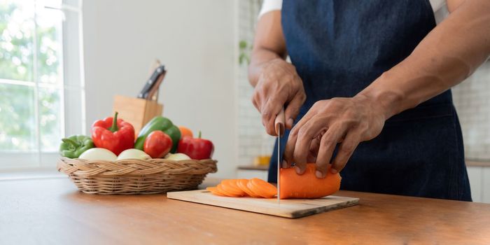 Man in kitchen looking at recipes on laptop while cooking.