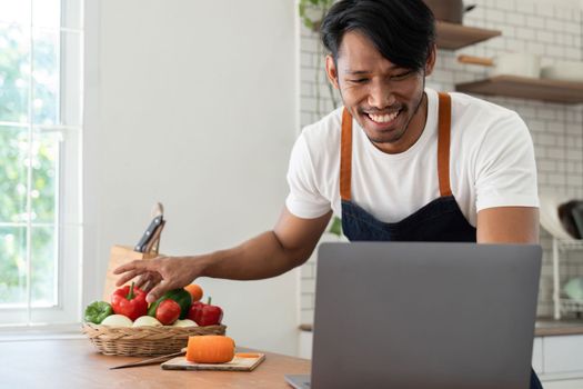 Man in kitchen looking at recipes on laptop while cooking.