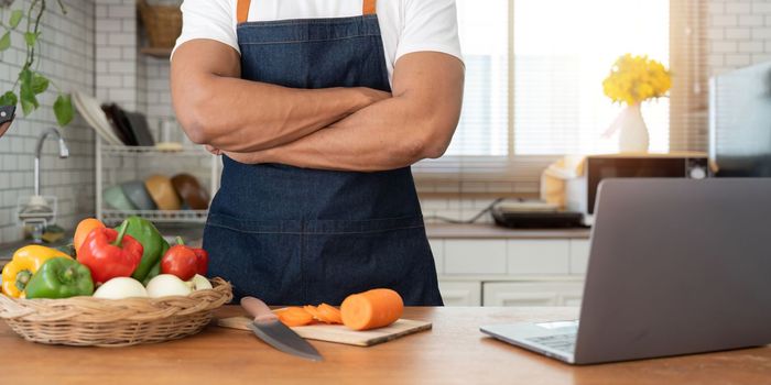 Man in kitchen looking at recipes on laptop while cooking.