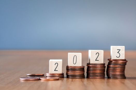 wooden cube year 2023 on top stack of coins with sky blue background and copy space. saving money and financial plan concept for investment in new year 2023. close up
