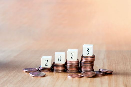wooden cube year 2023 on top stack of coins with sky blue background and copy space. saving money and financial plan concept for investment in new year 2023. close up