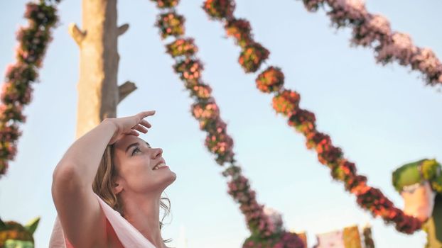 Girl on the background of hanging daisies of fresh flowers in a city park in Dubai